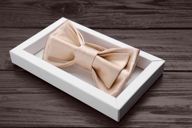 Stylish beige bow tie in box on wooden table, closeup
