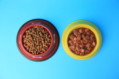 Photo of Wet and dry pet food in feeding bowls on light blue background, flat lay