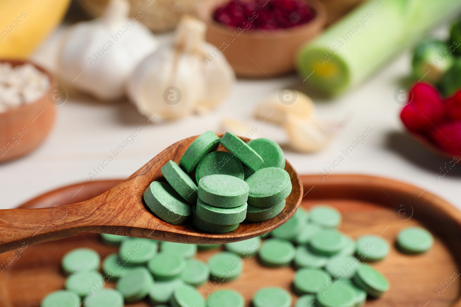 Photo of Holding spoon of prebiotic pills near table with food, closeup