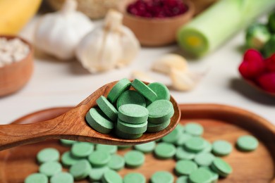 Photo of Holding spoon of prebiotic pills near table with food, closeup