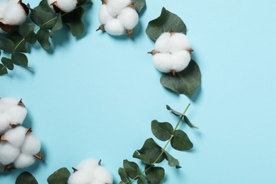 Photo of Frame of cotton flowers and eucalyptus leaves on light blue background, flat lay. Space for text