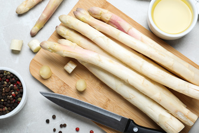 Photo of Fresh white asparagus, knife and cutting board on grey marble table, flat lay