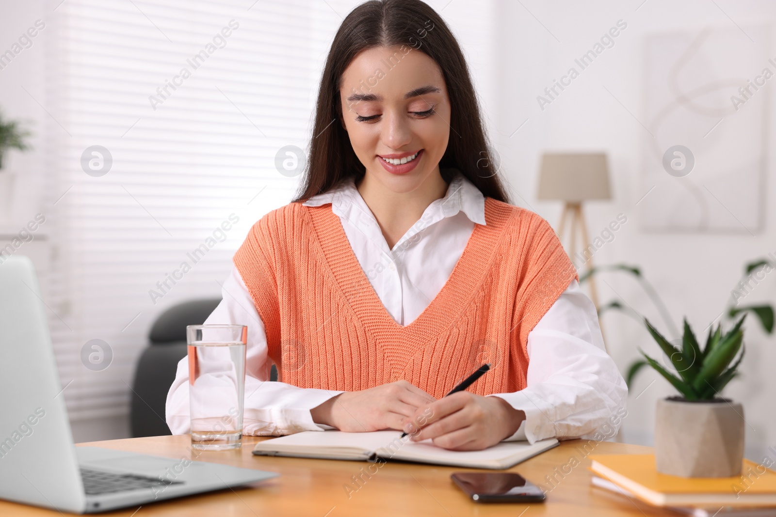 Photo of Young woman writing in notebook at wooden table indoors