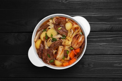 Pot of delicious vegetable soup with meat, noodles and ingredients on black wooden table, top view