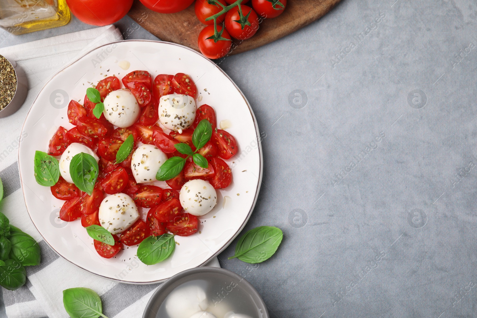 Photo of Tasty salad Caprese with tomatoes, mozzarella balls, basil and ingredients on grey background, flat lay. Space for text