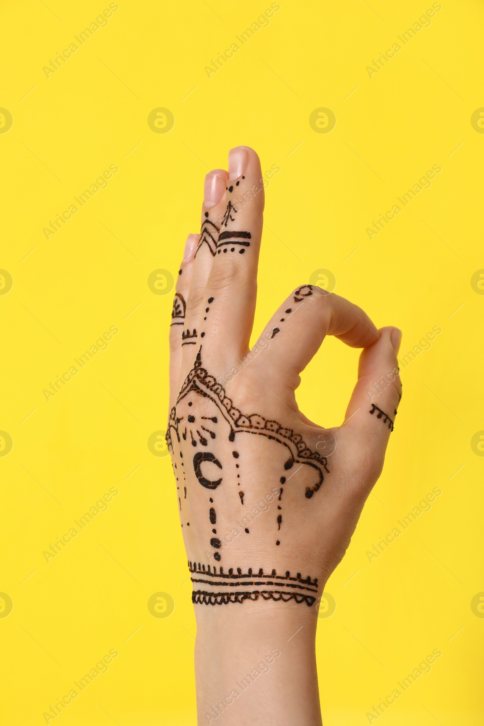 Photo of Woman with henna tattoo on hand against yellow background, closeup. Traditional mehndi ornament