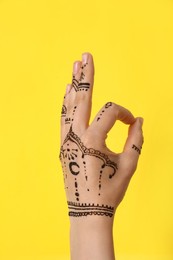 Photo of Woman with henna tattoo on hand against yellow background, closeup. Traditional mehndi ornament