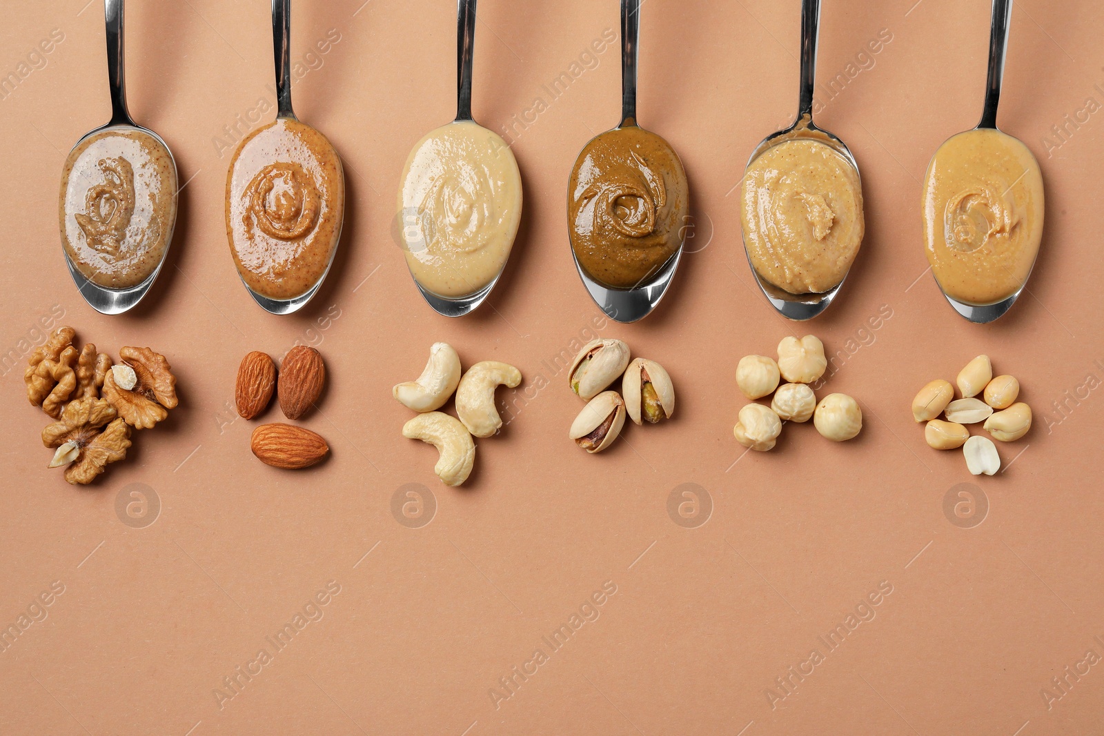 Photo of Tasty nut butters in spoons and raw nuts on light brown table, flat lay. Space for text