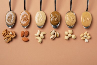 Photo of Tasty nut butters in spoons and raw nuts on light brown table, flat lay. Space for text