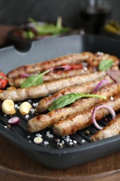 Grill pan with tasty sausages and vegetables on wooden board, closeup