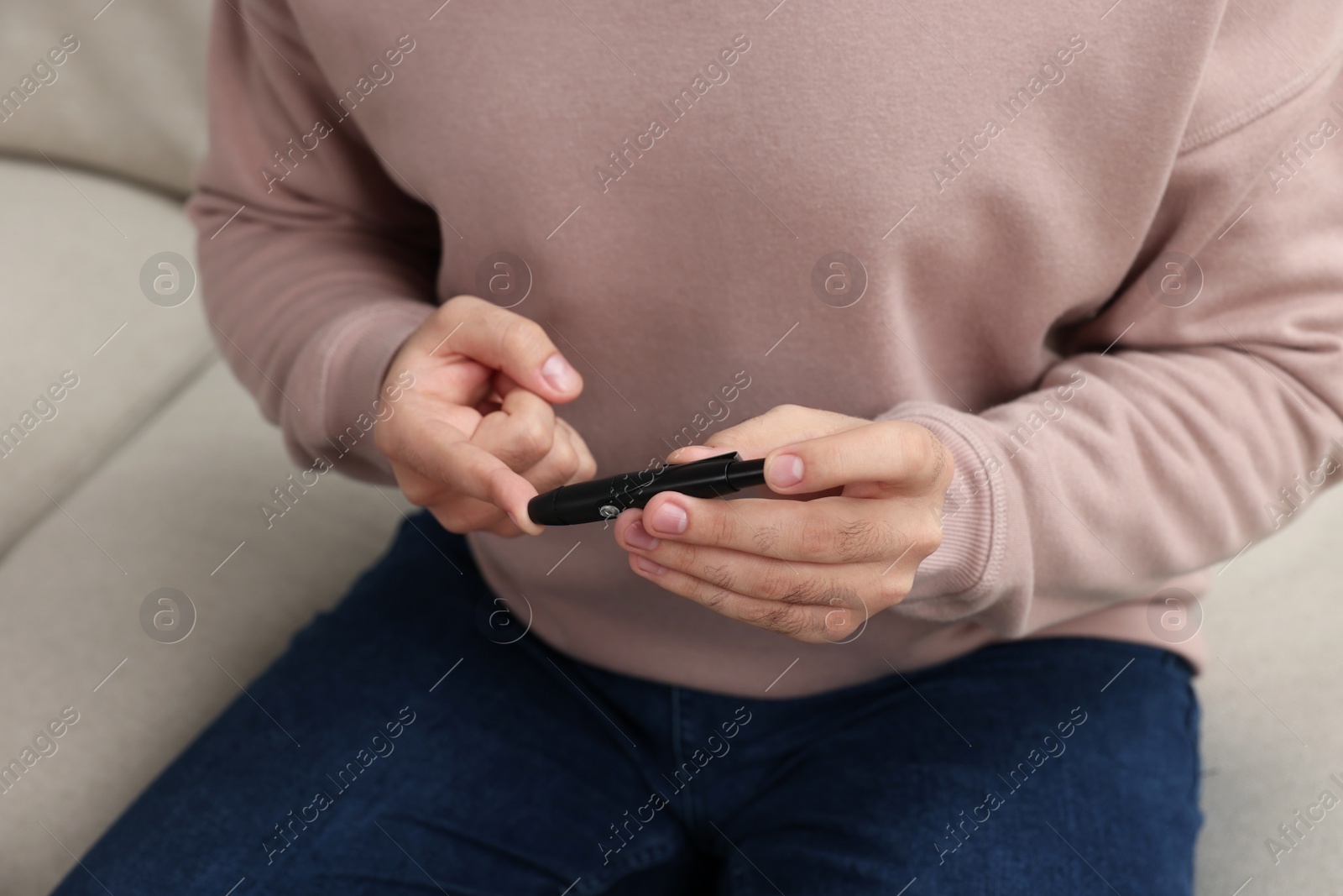 Photo of Diabetes test. Man checking blood sugar level with lancet pen on sofa, closeup