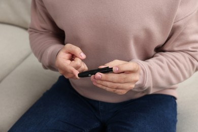 Diabetes test. Man checking blood sugar level with lancet pen on sofa, closeup