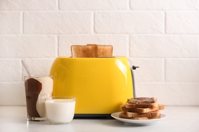 Modern toaster and delicious breakfast on table near brick wall