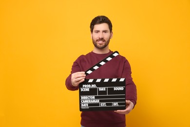 Photo of Smiling actor holding clapperboard on orange background, space for text