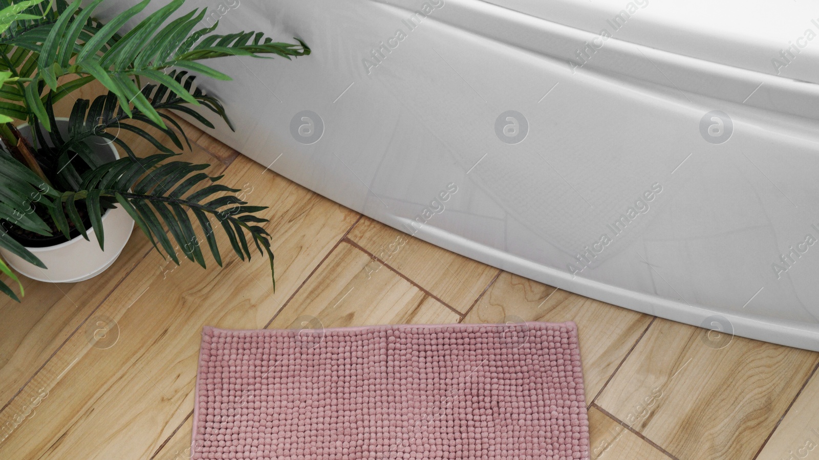 Photo of Soft bath mat near houseplant and tub on wooden floor in bathroom