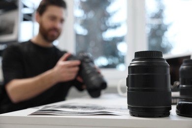 Photo of Professional photographer holding digital camera at table indoors, focus on lens