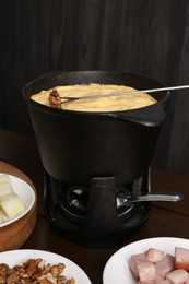 Photo of Fondue pot with tasty melted cheese, fork and different snacks on wooden table