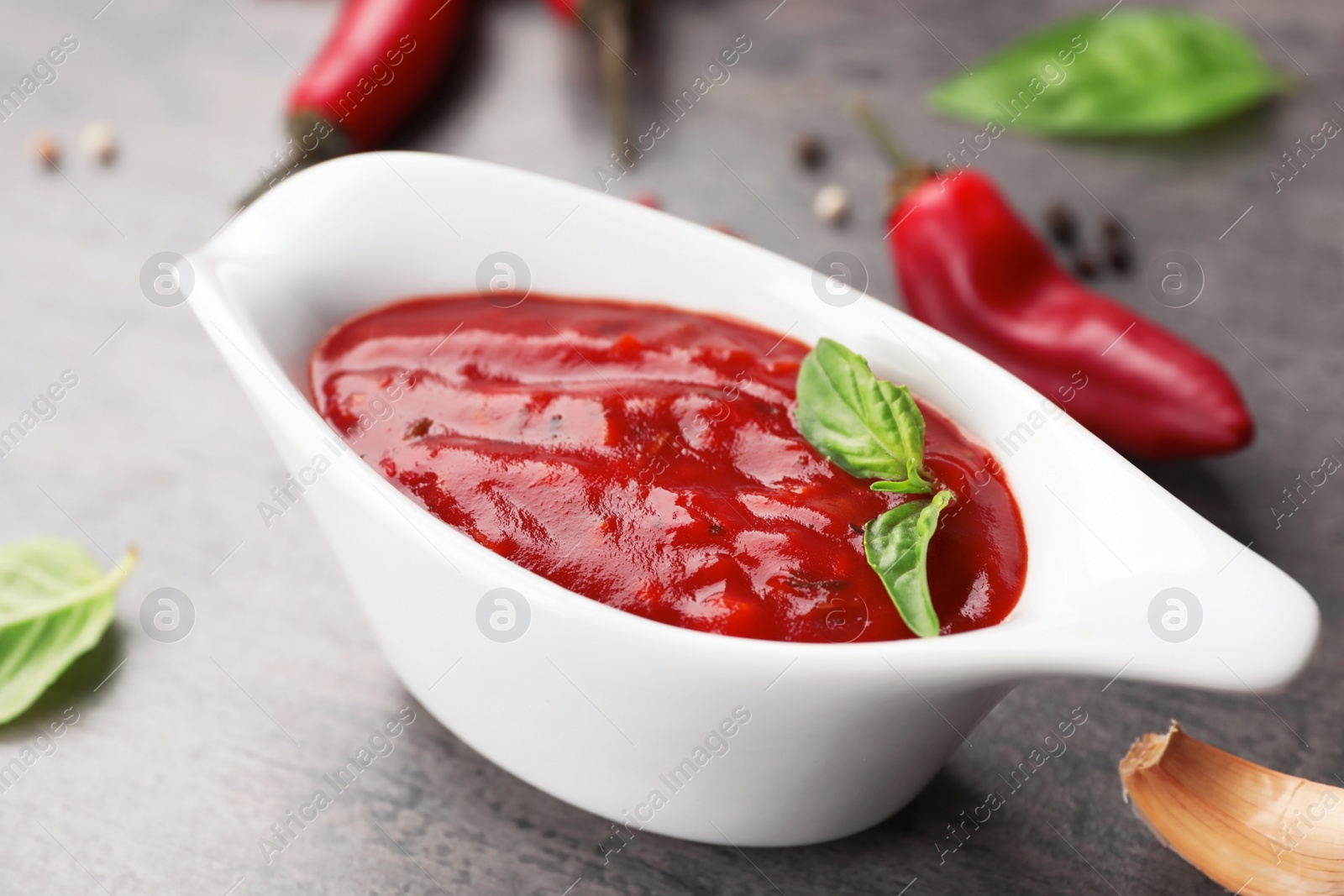 Photo of Gravy boat with spicy chili sauce on dark table