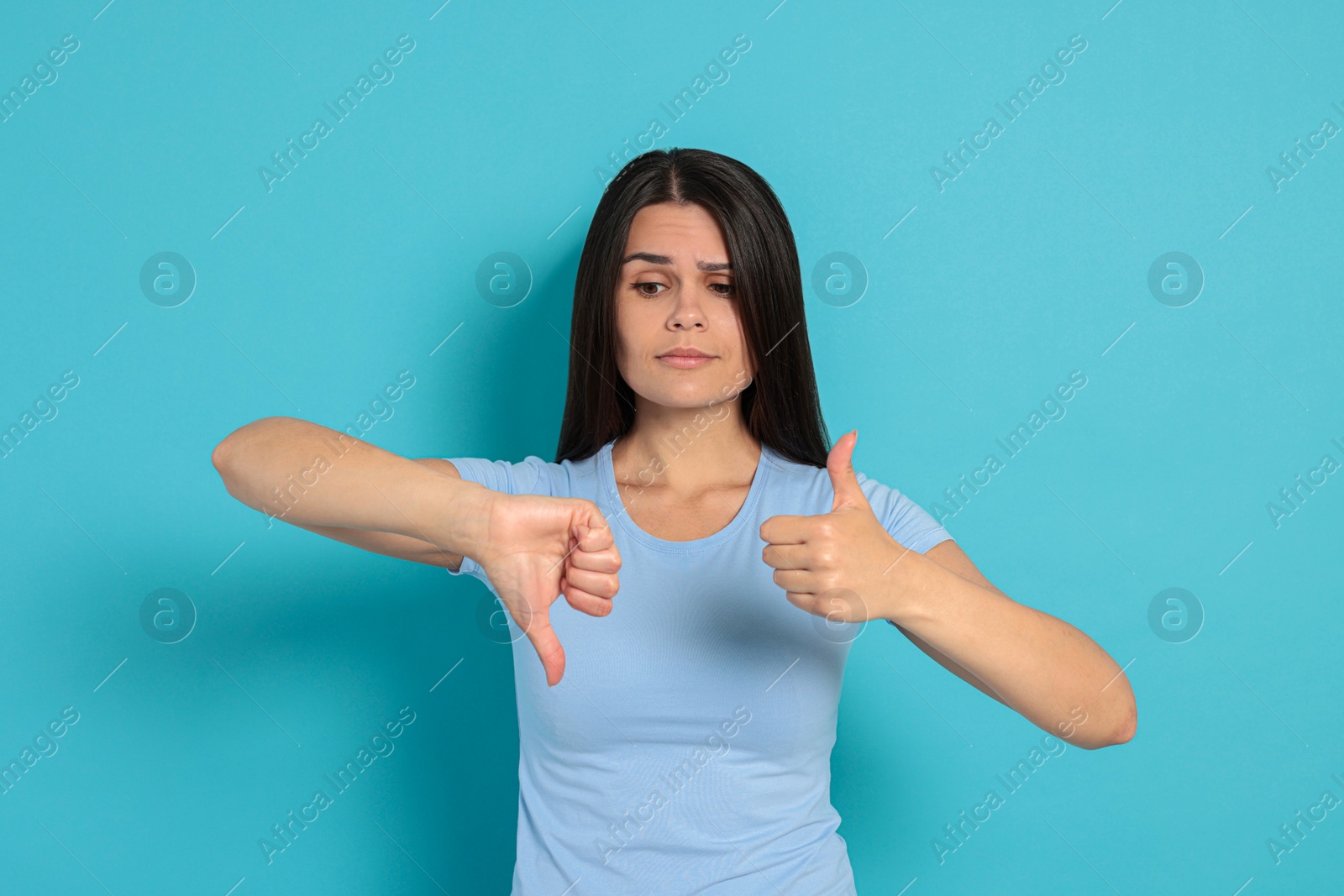 Photo of Young woman showing thumbs up and down on light blue background