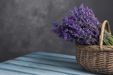 Beautiful fresh lavender flowers in wicker basket on wooden table against grey background. Space for text