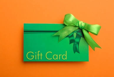 Gift card with bow on orange background, top view