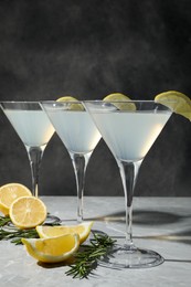 Photo of Martini glasses of refreshing cocktail decorated with lemon slices and rosemary on light grey textured table