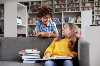 Photo of Happy little children reading book on sofa in library