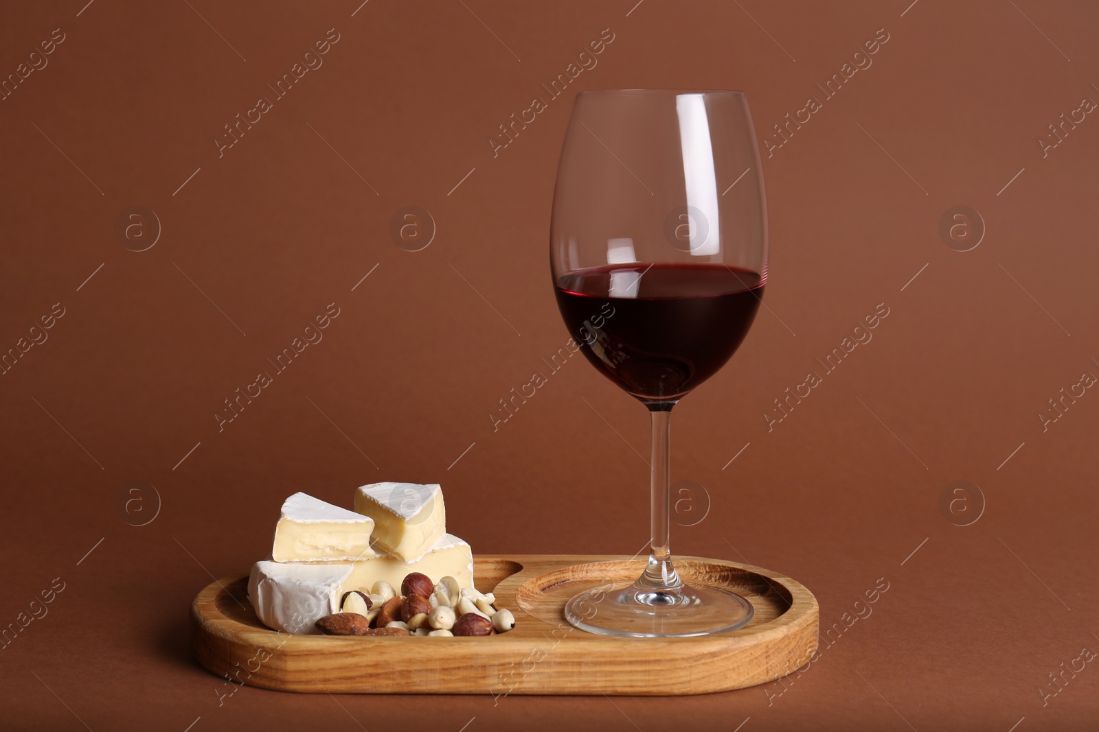 Photo of Glass of red wine, cheese and nuts on brown background