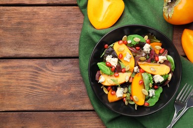 Delicious persimmon salad and forks on wooden table, flat lay. Space for text