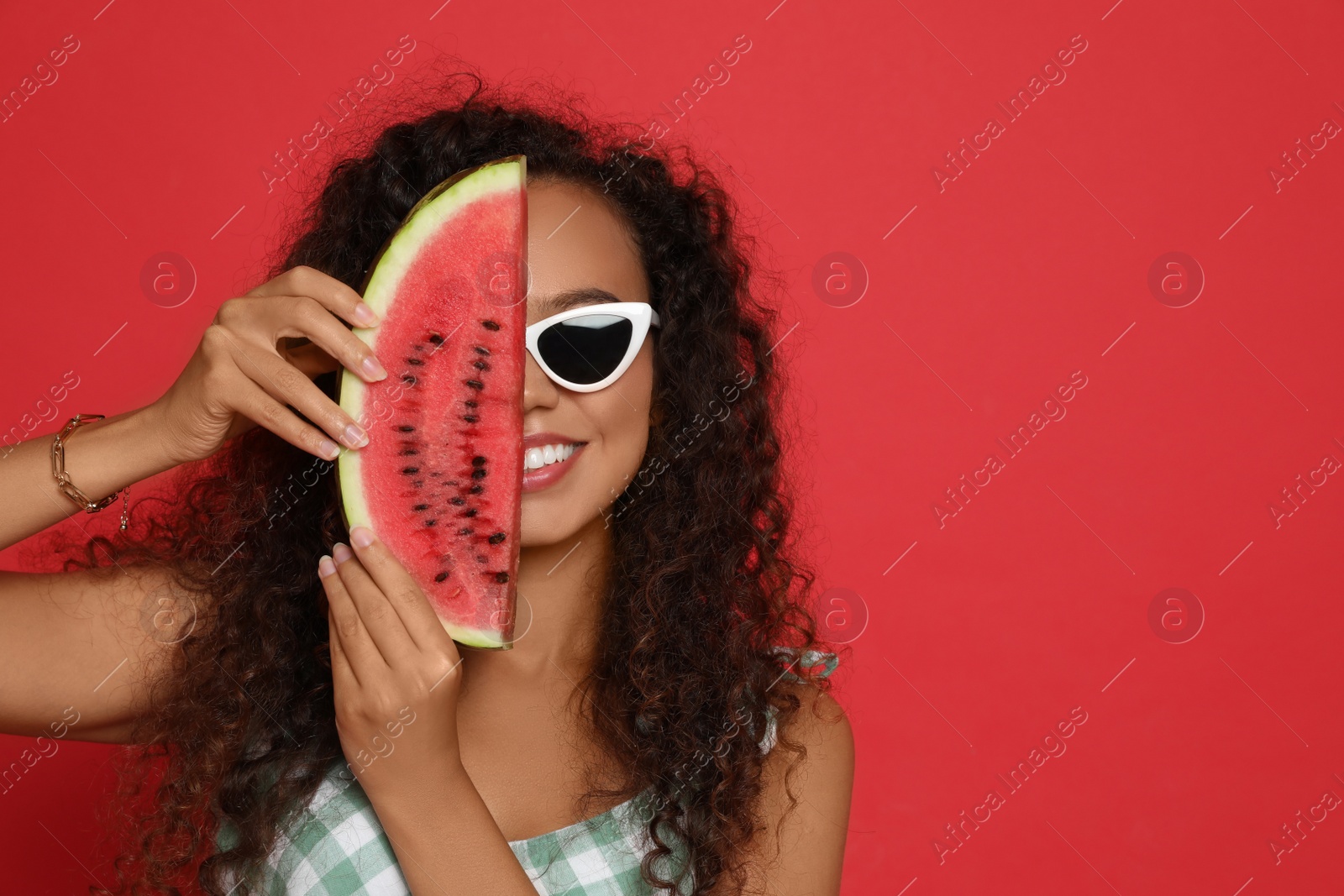 Photo of Beautiful young African American woman with slice of watermelon on red background. Space for text