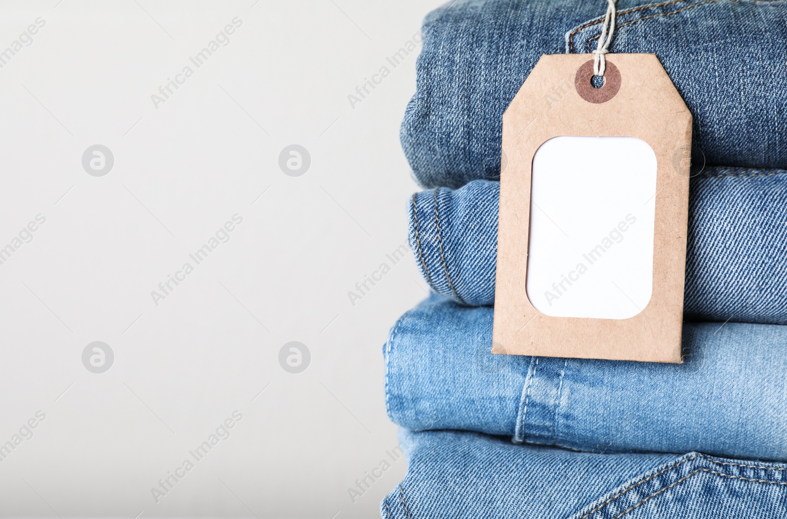 Photo of Stack of different jeans with tag on light background, closeup. Space for text