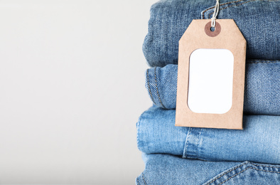 Stack of different jeans with tag on light background, closeup. Space for text