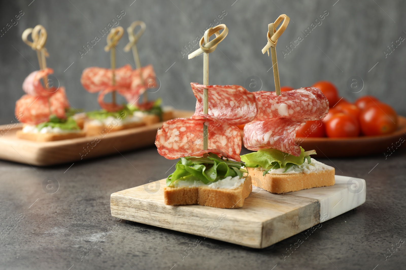 Photo of Tasty canapes with salami, greens and cream cheese on grey table, closeup