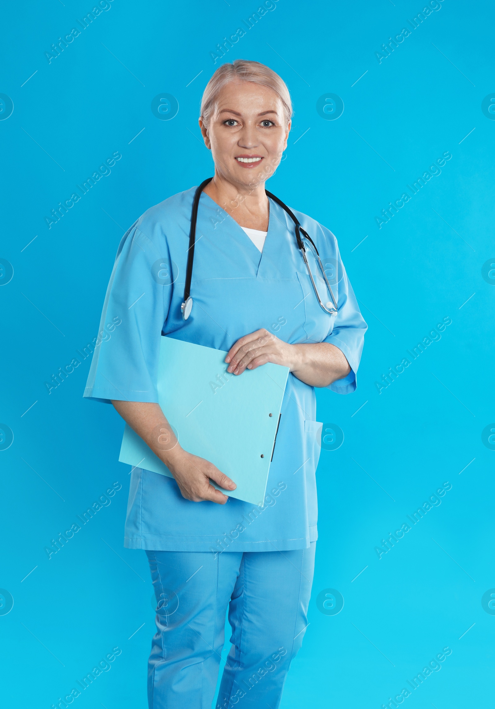 Photo of Mature doctor with stethoscope and clipboard on blue background