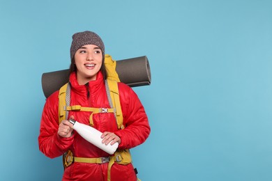 Photo of Smiling young woman with backpack and thermo bottle on light blue background, space for text. Active tourism