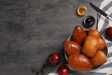 Delicious baked patties, apples, blueberries and jams on grey table, flat lay. Space for text