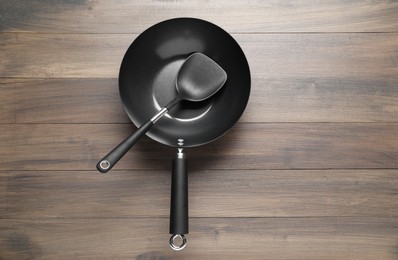 Photo of Black metal wok and spatula on wooden table, top view