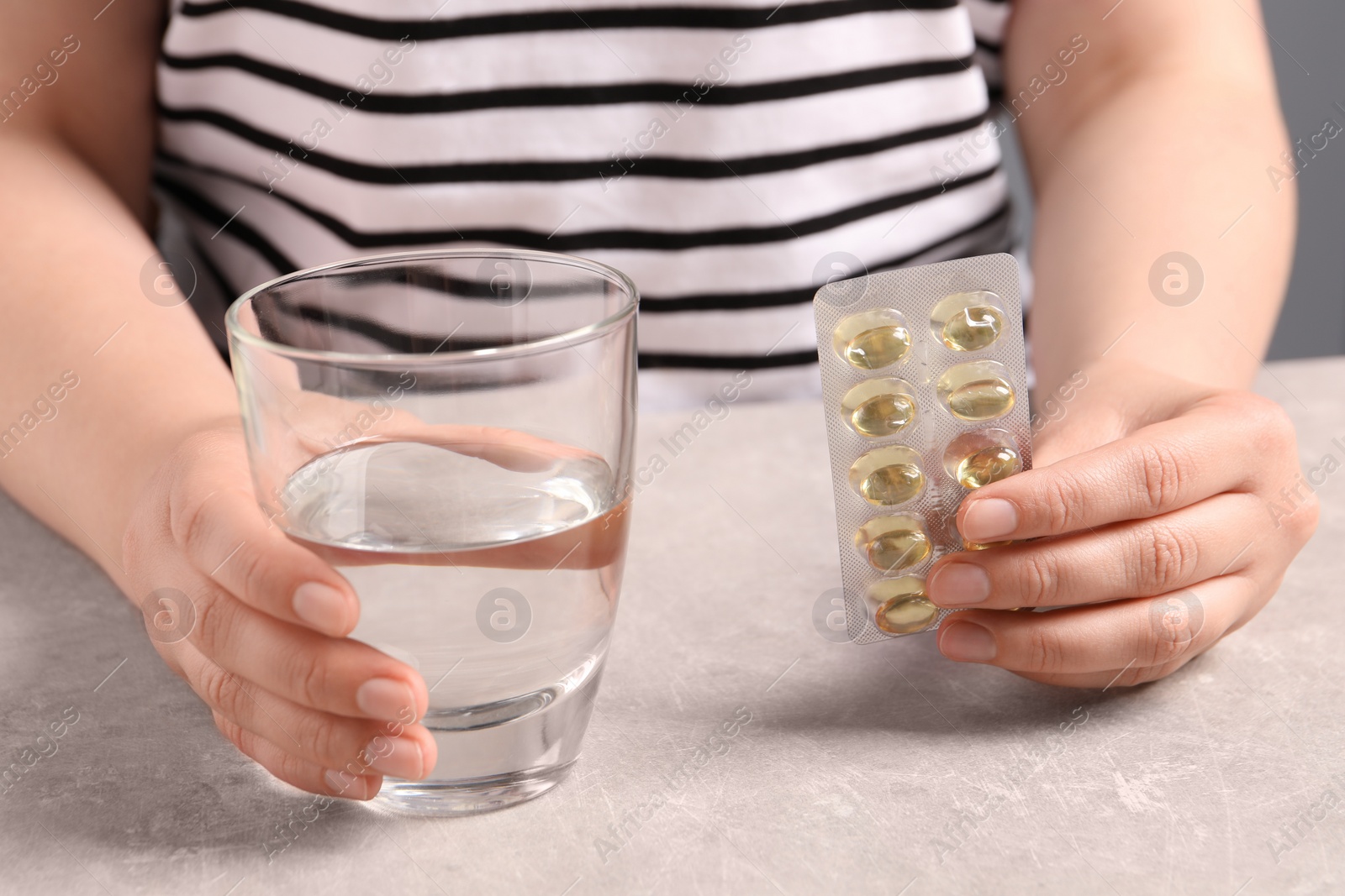 Photo of Woman with pills and glass of water at grey table, closeup