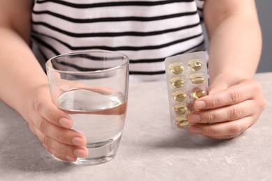 Woman with pills and glass of water at grey table, closeup