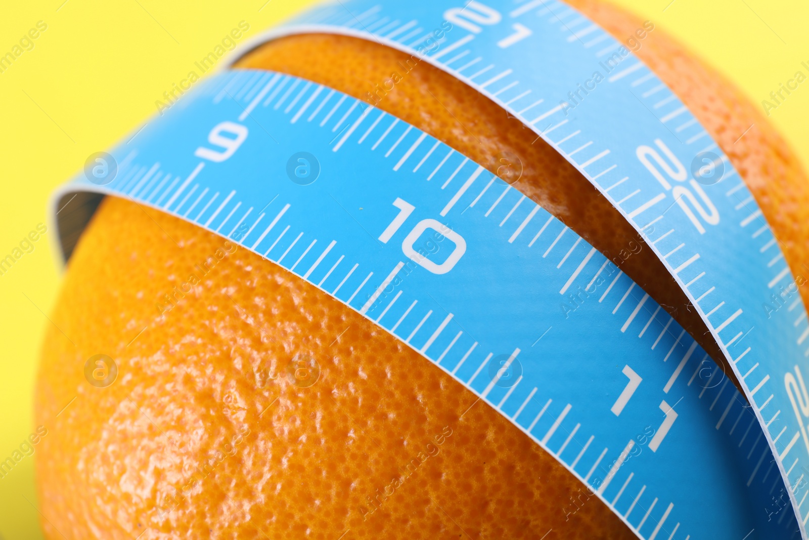 Photo of Cellulite problem. Orange with measuring tape on yellow background, closeup