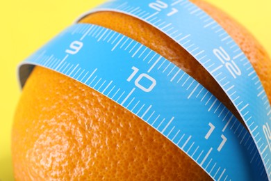 Photo of Cellulite problem. Orange with measuring tape on yellow background, closeup