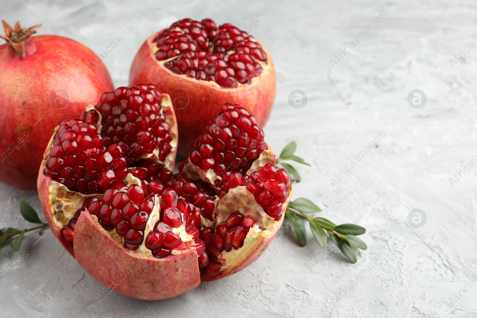 Photo of Fresh pomegranates and green leaves on grey textured table, closeup. Space for text