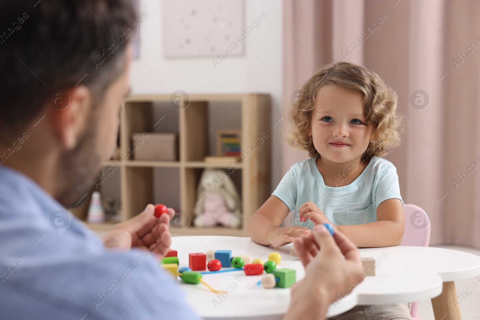 Photo of Motor skills development. Father and daughter playing with wooden lacing toy at table indoors