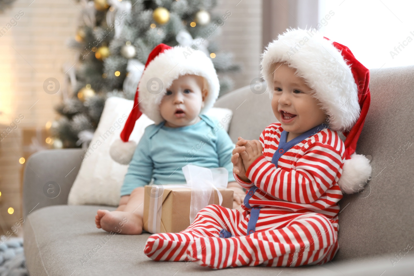 Image of Cute children in Santa hats sitting on sofa at home. Christmas celebration