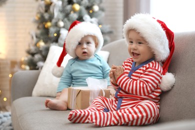 Image of Cute children in Santa hats sitting on sofa at home. Christmas celebration