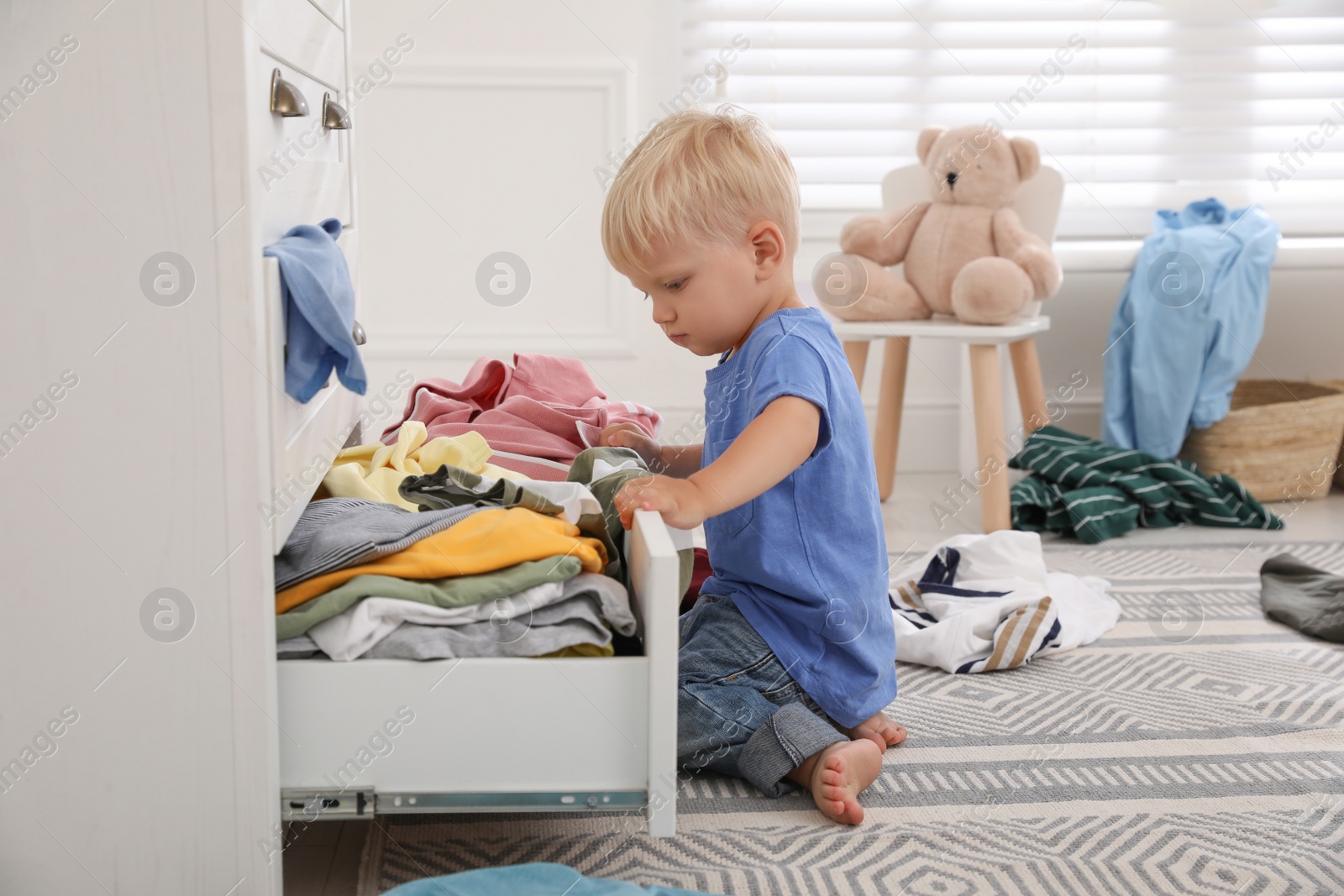 Photo of Cute little boy playing with clothes in dresser's drawer at home
