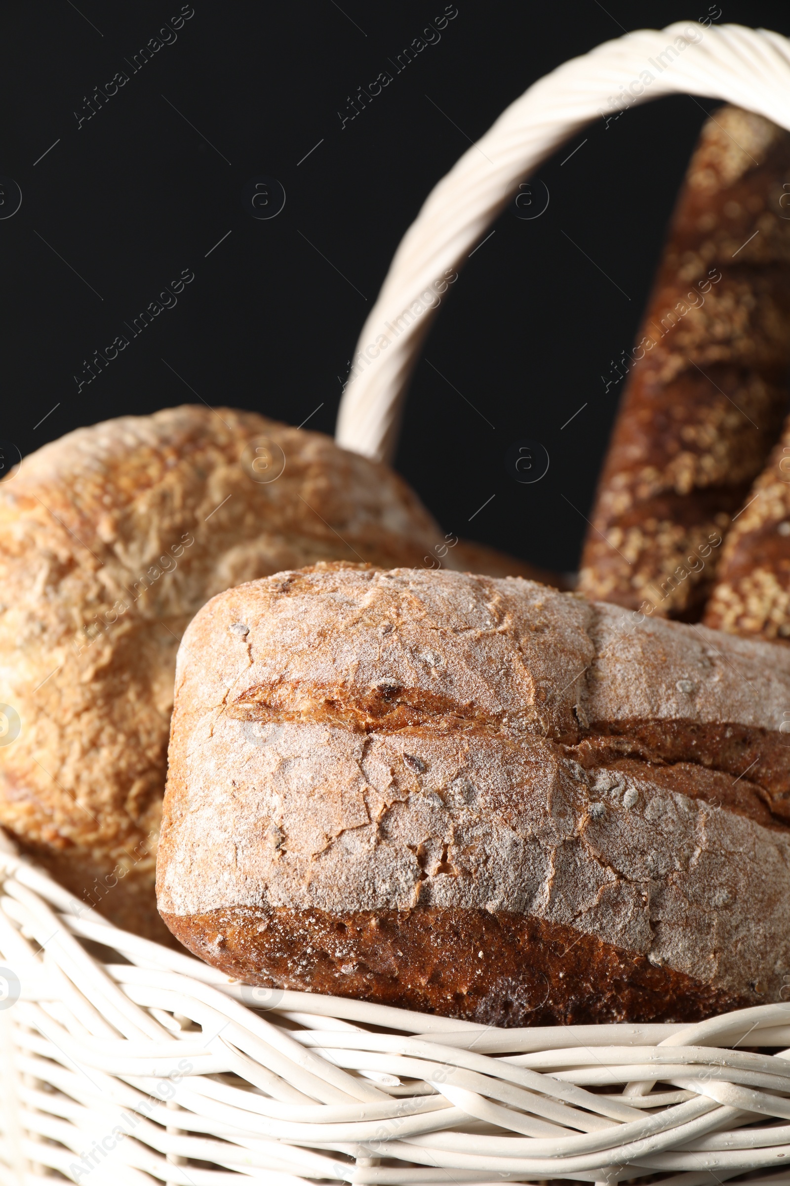 Photo of Wicker basket with different types of fresh bread on dark background, closeup