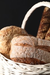 Wicker basket with different types of fresh bread on dark background, closeup