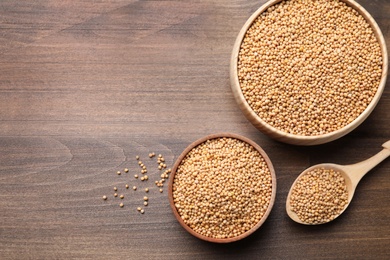 Mustard seeds in different dishware on wooden table, flat lay. Space for text