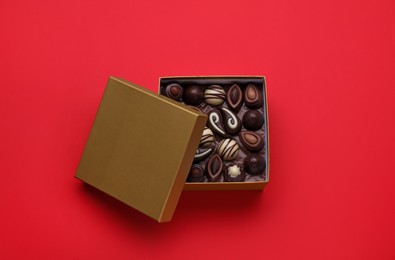 Photo of Open box of delicious chocolate candies on red background, top view